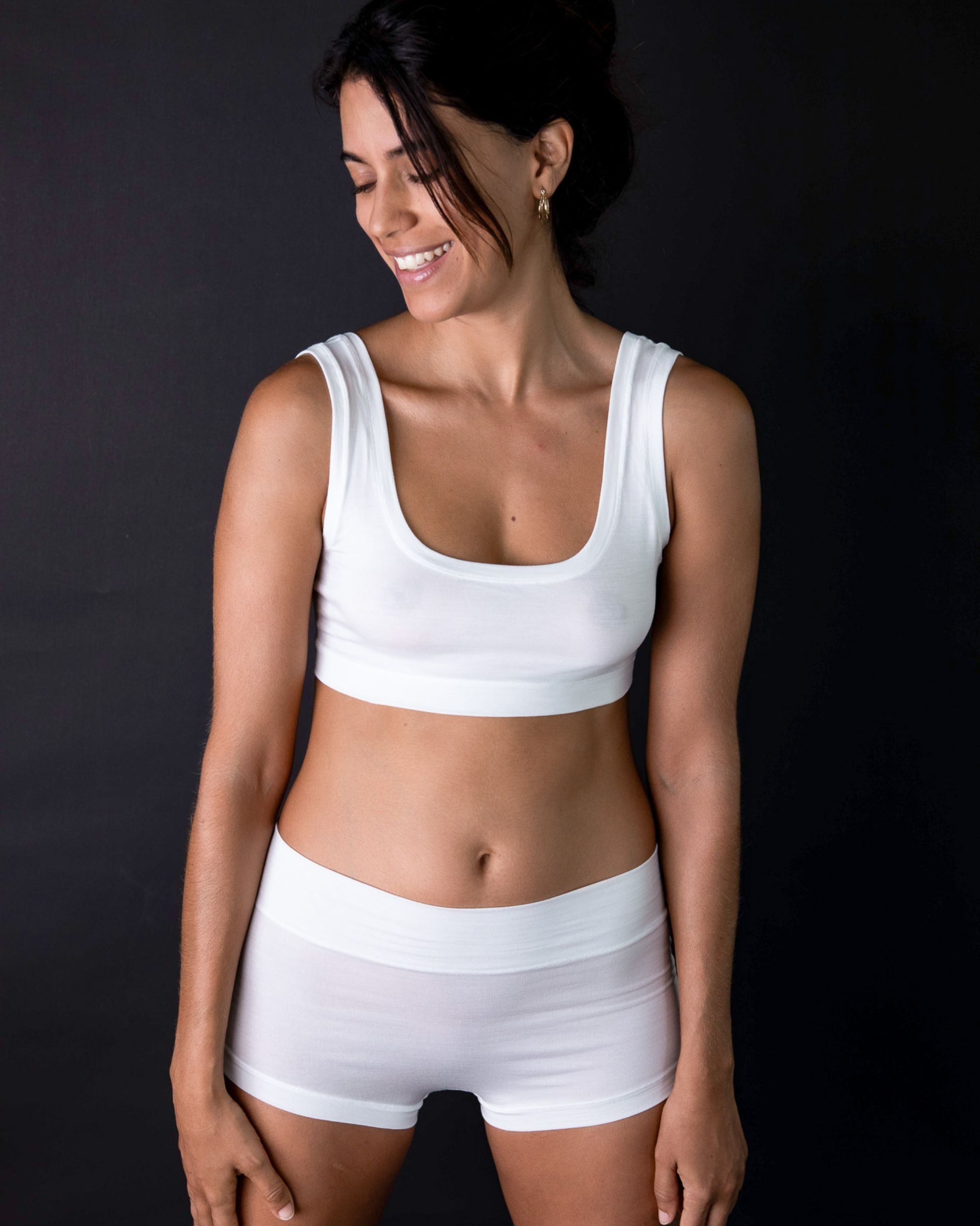 Woman wearing a white sports bra and shorts on a black background