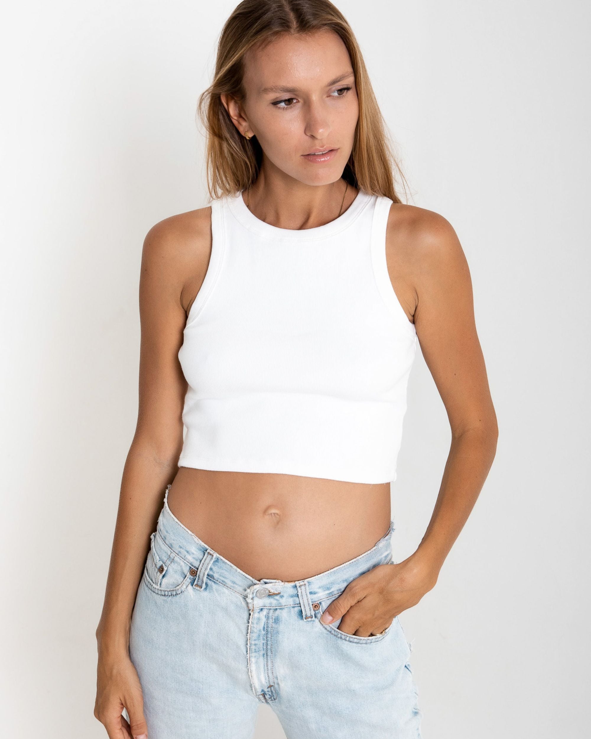 Woman wearing a white sleeveless top and light blue jeans on a plain background