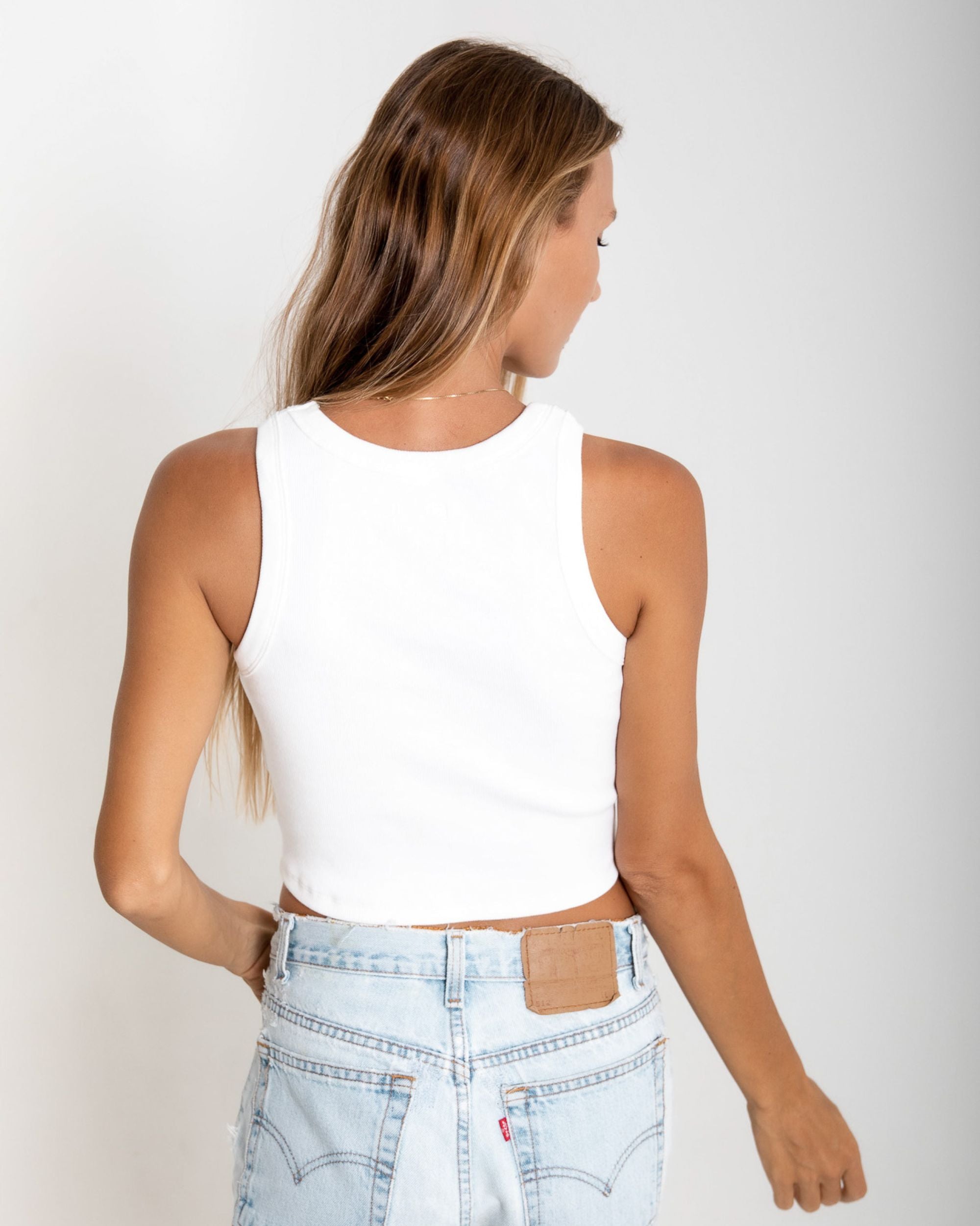 Woman wearing a white sleeveless top and light blue jeans on a plain background